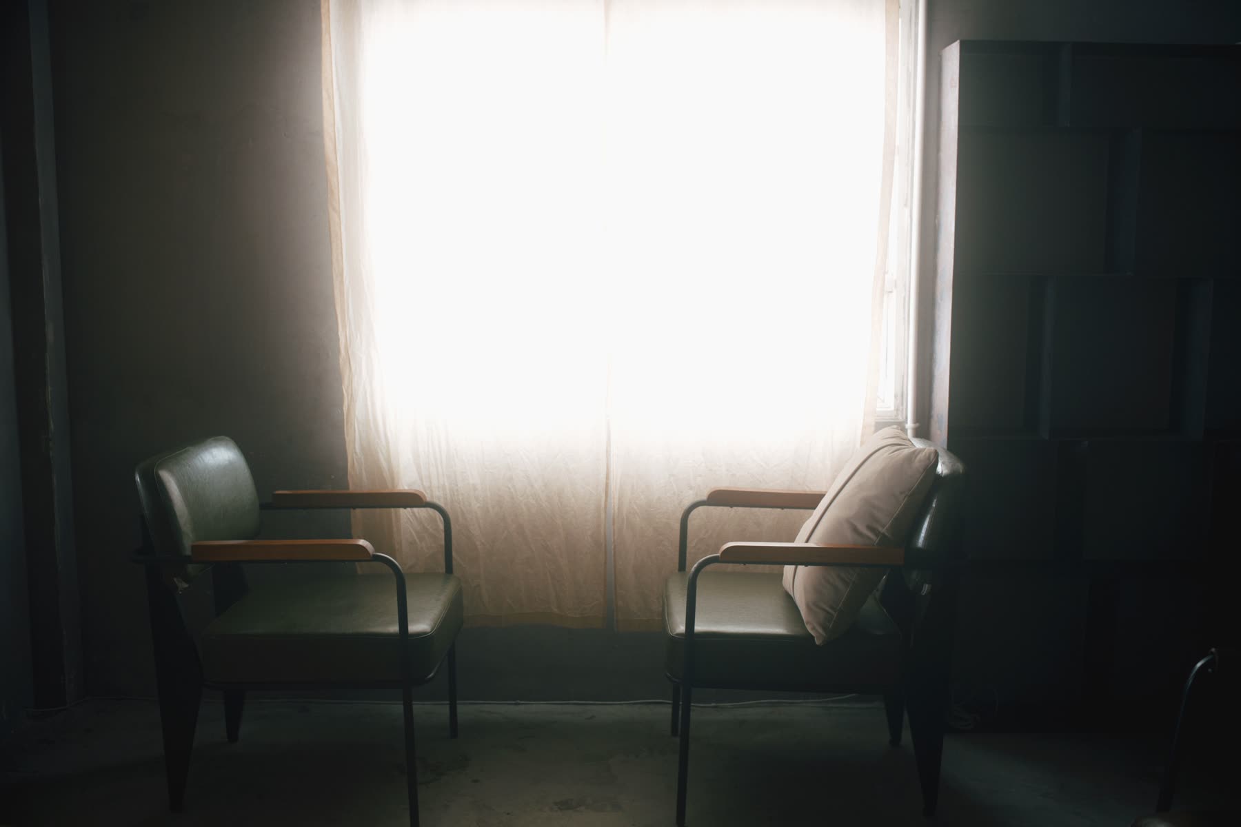 Two empty armchairs facing each other in front of a curtained window in a dim room.